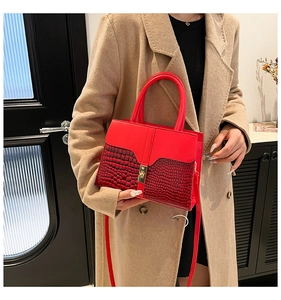 Détail du sac rouge avec texture crocodile et boucle dorée sur manteau en laine camel