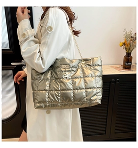 Close-up of quilted silver tote bag with golden chain and deer pendant on white coat