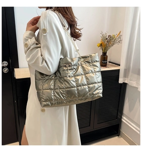 Detail of quilted silver tote bag with gold chain strap and cat charm on white coat
