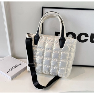 Detail of quilted waterproof fabric and contrasting black leather handles on white tote bag