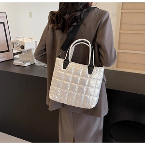 Detailed view of a white quilted tote bag with black straps on a person outdoors