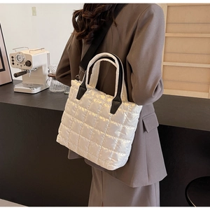Close-up of a white quilted puffer tote bag featuring black leather handles and shoulder strap