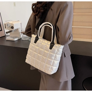 Detail of white quilted nylon tote bag showing wide black shoulder strap and texture