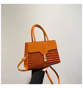Close-up of orange faux crocodile skin texture and gold buckle on a stylish handbag