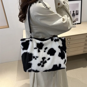 Borsa tote in peluche con stampa mucca e tracolle nere indossata su un cappotto beige