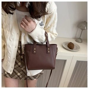 Detail of a dark brown vintage tote bag with gold rivets and detachable crossbody strap