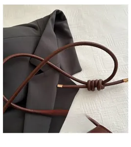 Close-up of a brown leather shoulder bag handle with woven knot and gold hardware