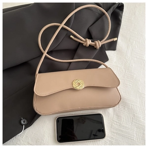 Flat lay of a beige leather shoulder bag with a gold circular buckle on a black blazer
