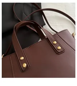 Close-up of matte brown leather tote bag with gold rivet accents and neat stitching