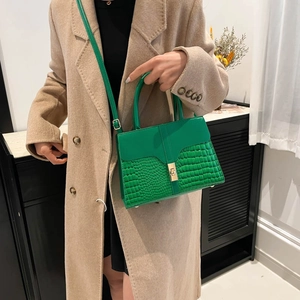 Green leather tote bag with crocodile texture and gold lock shown on a female model
