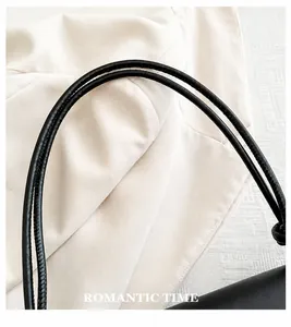 Dettaglio del manico in pelle nera e cuciture precise su una borsa a tracolla minimalista