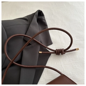 Detail of dark brown leather shoulder strap with elegant knot and gold metal tips