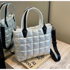 Detail of white quilted puffer tote bag with black leather handles and nylon strap