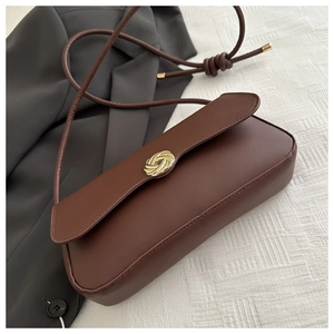 Detail of a brown leather shoulder bag featuring a golden knotted metal buckle and strap