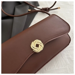 Close-up of brown leather handbag featuring a stylish golden spiral knot metal buckle