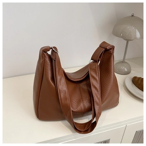 Caramel brown pebble leather hobo bag with dual shoulder straps on a clean white desk