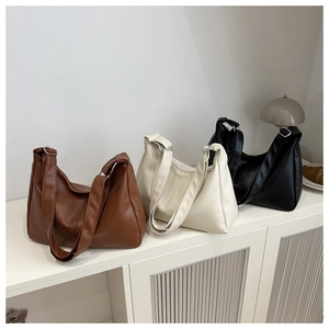 Trio of large leather hobo bags in brown, cream, and black displayed on a white shelf