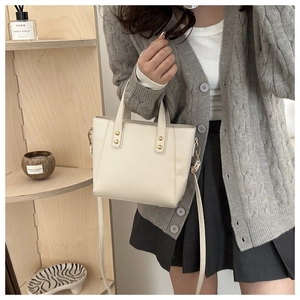 Detail of cream white tote bag with gold rivets, worn by model in a cozy lifestyle setting