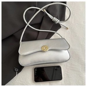 Metallic silver crossbody bag with golden knot clasp and smartphone for size reference
