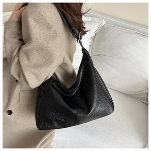 Close-up of black textured leather hobo bag with adjustable strap on beige suit