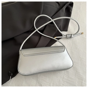 Detail of silver metallic underarm bag with knotted strap on a black blazer background