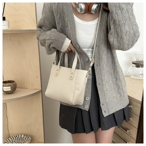 Beige leather tote bag with gold hardware shown on a model in a cozy lifestyle setting