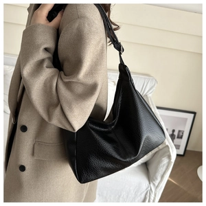 Detail of black pebbled leather hobo tote bag worn with a beige cashmere coat