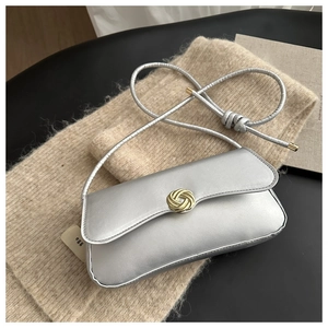 Detail of silver matte baguette bag with gold knot buckle on beige knit sweater