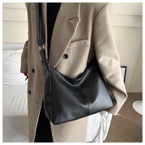 Detail of black pebbled leather tote bag worn as a shoulder bag on a beige coat