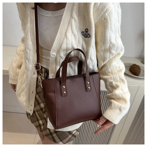 Detail of vintage brown PU leather bucket bag with gold rivets on knit cardigan