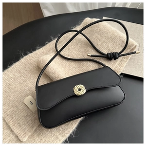 Detail of minimalist black baguette bag with gold spiral knot buckle and sleek leather