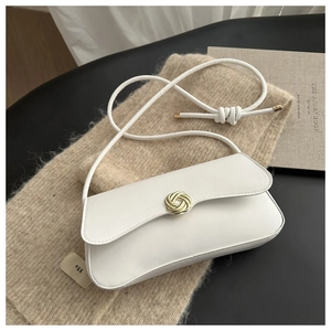 Detailed macro view of white shoulder bag featuring a golden knot buckle and slim strap