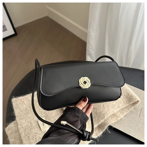 Detail of black leather shoulder bag with golden round floral clasp and knotted strap