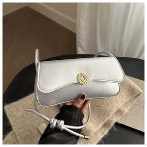 Detail of silver faux leather shoulder bag with a gold woven knot buckle and knotted strap