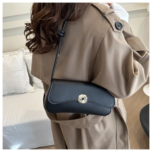 Chic black leather shoulder bag with gold woven buckle on a model in a trench coat