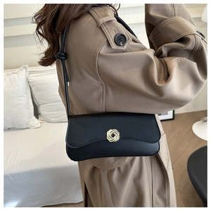Detail view of black leather shoulder bag with golden round flower lock on khaki coat