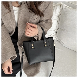 Detailed look at black matte leather tote bag with gold rivets worn on shoulder