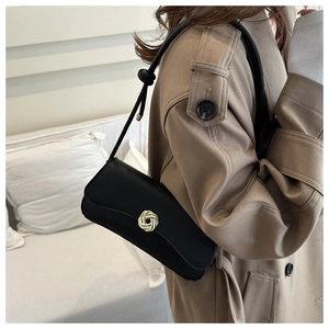 Detail of a black leather underarm bag with golden knot clasp worn over a khaki trench coat