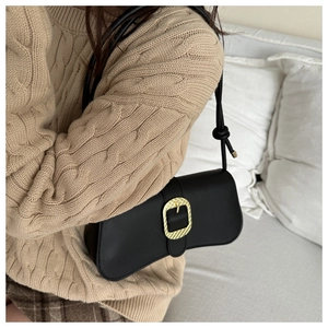 Detalle de un bolso baguette de cuero negro con una hebilla de metal dorado chic
