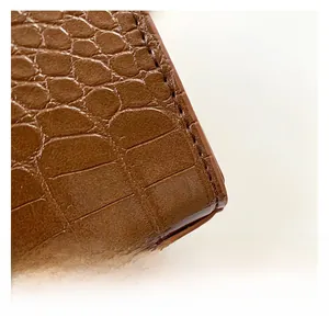 Macro detail of brown crocodile embossed leather with precise stitching on shoulder bag