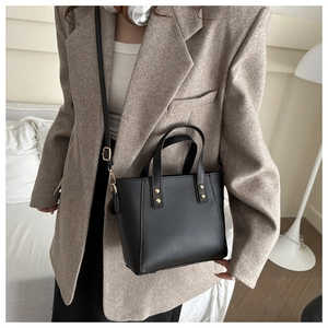 Minimalist black tote bag with gold studs shown styled on a model in a modern room