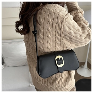 Detalle de bolso negro con hebilla dorada de herradura sobre un suéter beige de punto