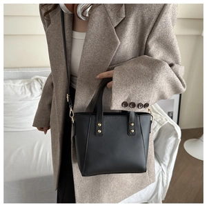 Detail of black leather tote bag with gold studs and detachable shoulder strap on model