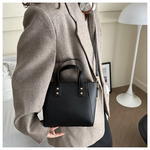 Close-up of black leather bucket bag with gold studs worn over a brown wool blazer