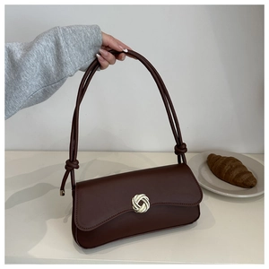 Detail of a dark brown leather underarm bag featuring a metallic knot buckle and handle