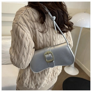 Detalle de bolso de hombro plateado con hebilla dorada texturizada y nudo decorativo