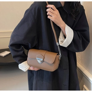 Gros plan du sac bandoulière en cuir marron avec fermoir triangulaire argenté sur mannequin