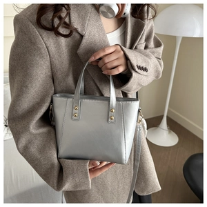 Detail of silver tote bag with gold rivets worn by a model in a brown suit for office commuting