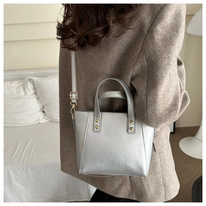 Silver metallic tote bag detail with golden rivets and adjustable strap on a shoulder