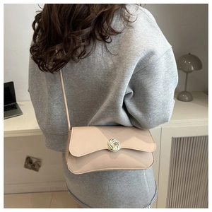 Detail view of beige crossbody bag featuring a golden woven circular metal lock and strap